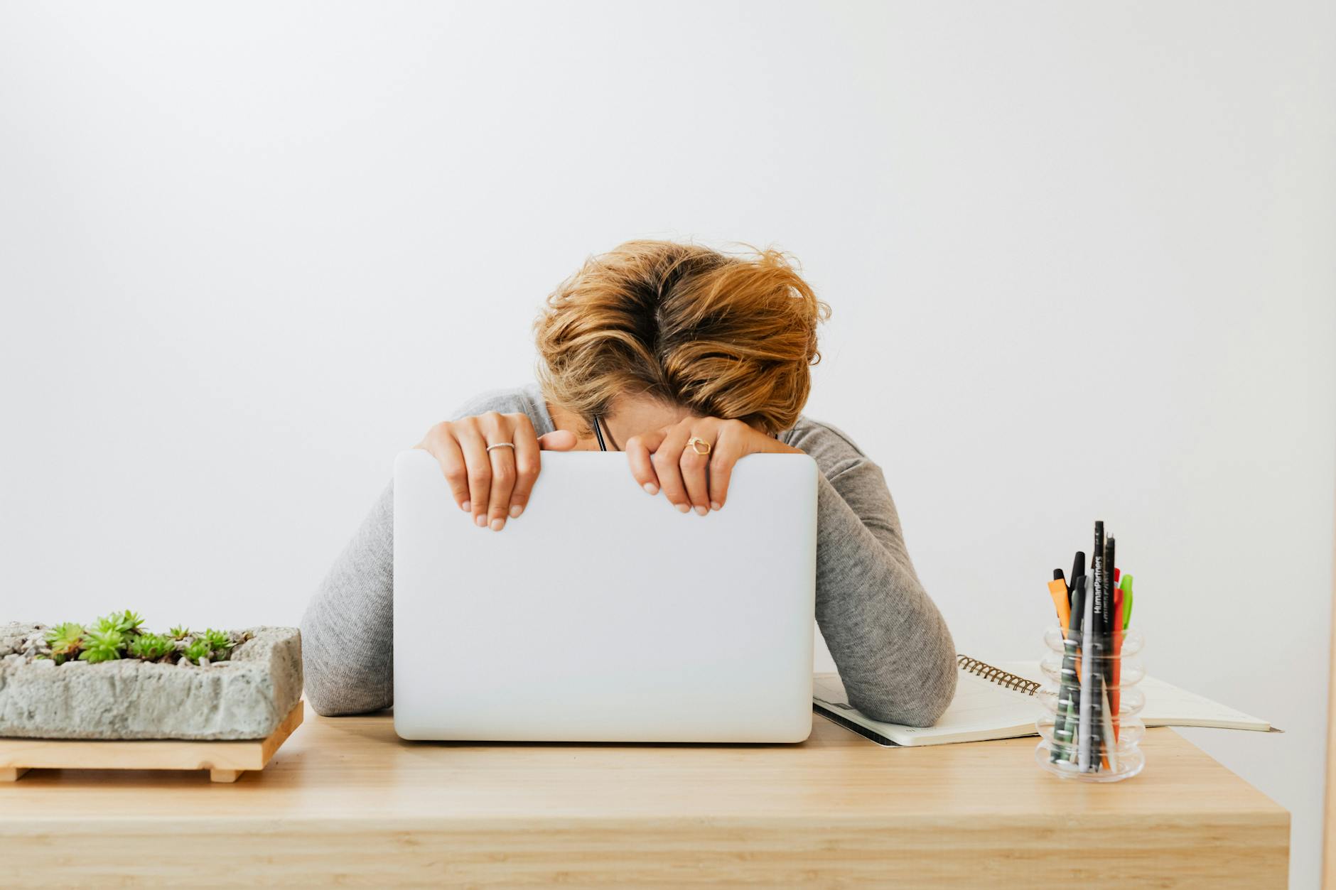 a woman leaning and holding onto a laptop on a wooden table